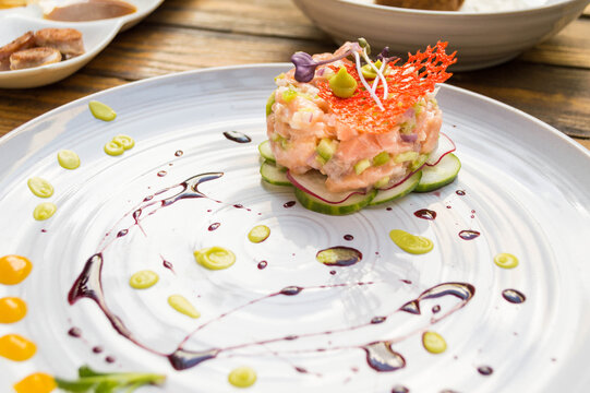 Tartar  de salm&oacute;n gourmet  sobre cama de pepino y rabano, decorado con brotes de albahaca coral de zanahoria y reduccion de vino tinto, aguacate y fruta de la pasion. Primer plano.