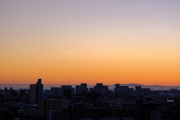 Fototapeta na wymiar 都市の夜明け、早朝ビルの隙間から太陽が昇り辺りはオレンジ色に染まる。ビルはシルエットに浮かぶ