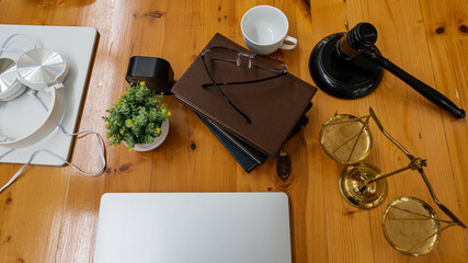 Tablet and eyeglasses and notebook with coffee cup and audio headphones with gold hammer and scales on business man's desk.