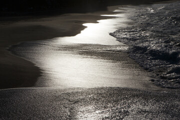 Sunset sunlight reflecting on the wave-wet beach sand © Imaxepress