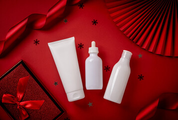 White bottles cosmetic products with red ribbon and Christmas decoration on red background....