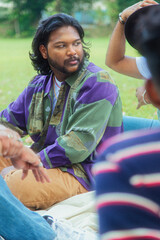 Malaysian Indian men in a group against a cloth backdrop in a park surrounded by trees, talking,...
