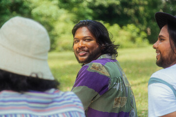 Malaysian Indian men in a group against a cloth backdrop in a park surrounded by trees, talking, laughing and sitting together