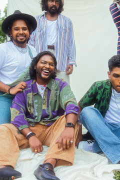 Malaysian Indian men in a group against a cloth backdrop in a park surrounded by trees, talking, laughing and sitting together