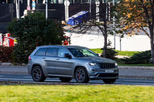 Moscow; Russia - October 13; 2021: silver Jeep Grand Cherokee   is driving fast on the street on a warm autumn day against the backdrop of a  park