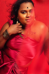 Malaysian Indian individual dressed in red clothing, against a red background, posing and laughing