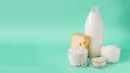 A set of dairy products in close-up on a light green background of the copy space. Milk, kefir, sour cream, cheese, butter and cottage cheese in a transparent bowl on a light background