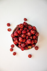 Sun-dried wild rose hip in a white bowl on white background