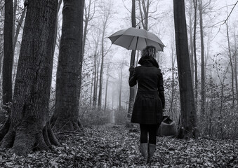 A lonely woman is walking in the forest with an umbrella