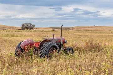 Poster Vintage red tractor abandoned in tall grass on the prairies in Saskatchewan © Nancy Anderson