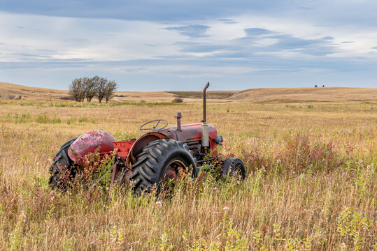 Vintage red tractor abandoned in tall grass on the prairies in Saskatchewan