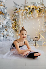 a beautiful delicate ballerina in a fluffy white skirt on the side of a decorated Christmas tree