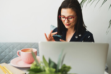 Beautiful woman sits in a cafe, drinks coffee, works on a computer and uses a phone