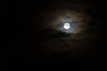 Full moon shining glowing light through the darkness of cloudy night sky; long exposure for...