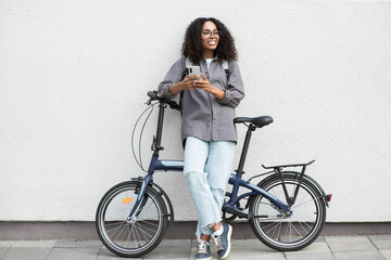 Obraz na płótnie Canvas Young woman with bicycle over white wall background in city, Smiling student girl with bike smiling outdoor using mobile phone, Modern healthy lifestyle, travel, casual business concept