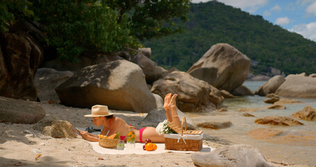 Young woman in red bikini is sunbathing on lonely beach, enjoying the sun and playing on the phone