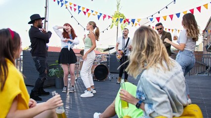 Attractive smiling young carefree women drinking beer and making selfie during summer party on terrace. Friends having fun and dancing on a rooftop party. - Powered by Adobe