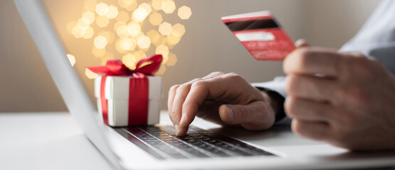 Man hand holding credit card and using laptop computer ordering Christmas gift panoramic banner,...