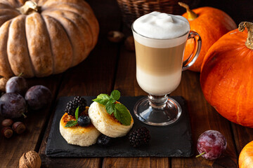 Two cheesecakes decorated with berries and mint leaves. There is a glass of coffee on the table and there are various vegetables.