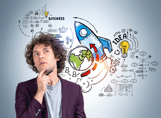Businessman thinking with pen in hand, start up sketch with rocket on grey wall