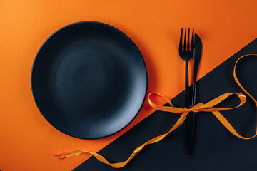 Halloween table setting with an empty black plate and cutlery a black and orange background.