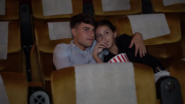 Happy young couple watching scary movie film and hand cover eye to Shocked and eating popcorn and embracing together in cinema of  theater