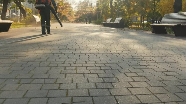 A man in a park with a blower removes dust and autumn leaves.