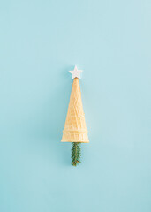 Creative Christmas tree idea made of ice cream cone, a wooden star and a pine twig on a blue background. Minimal flat lay, New Year concept. Christmas food inspiration.