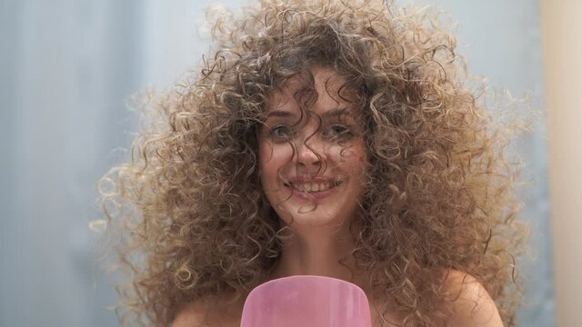 Close-up of a woman with Afro curls, her hair is fixed with hairspray. She laughs covering her face with a plastic protective screen. High quality 4k footage