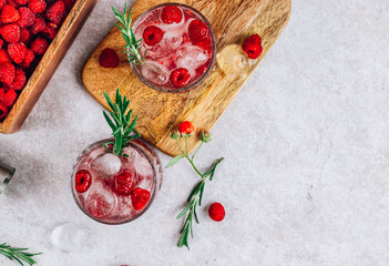 Raspberry lemonade in a glass with ice and fresh rosemary on a stone background.