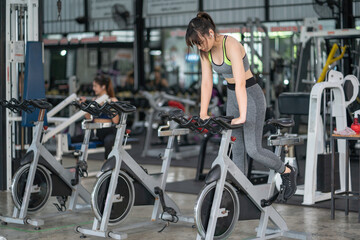 Fototapeta na wymiar Beautiful Asian woman exercising on stationary cycling machine in indoor fitness gym