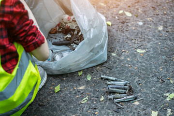 volunteer cleaning up used syringe in park and standing by bunch of garbage bag