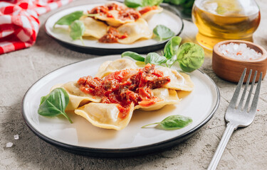Italian ravioli with meat tomato sauce and basil leaves with on a white dishes on concrete background.