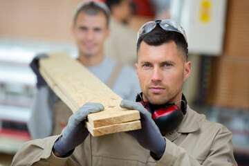 two craftsmen carrying a piece of wood