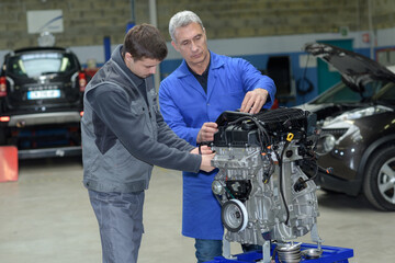 auto mechanic shows trainee maintenance of car engine