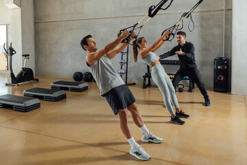 Personal trainer assists a couple that work out with elastic resistant strap.