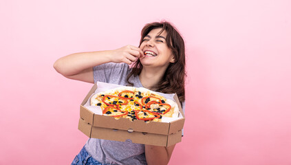 Attractive girl with pizza in a box for delivery on a pink background.