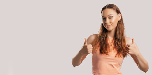 Beautiful young girl smiling and shows thumbs up gesture with two hands on a white isolated background. Positive woman points to an idea, a place for advertising