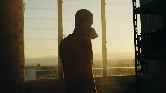 Sagoma di un uomo che beve una tazza di the alla finestra al tramonto.