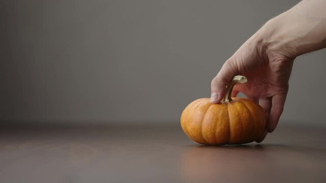 Slow motion man hand take small orange pumpkin from walnut table with copy space