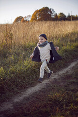 Naklejka na ściany i meble boy in warm clothes runs along a path on a field with dried grass