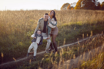 family of three with a boy child mom and dad are standing on a field in autumn at sunset