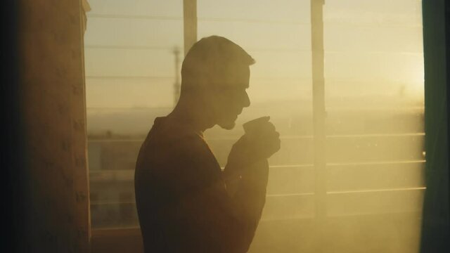 Sagoma di un uomo che beve una tazza di the alla finestra al tramonto.