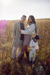 family of three with a boy child mom and dad are standing on a field in autumn at sunset