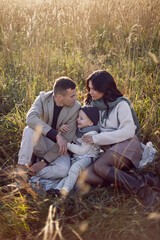 Naklejka na ściany i meble family of three with a boy child mom and dad are sit on a field in autumn