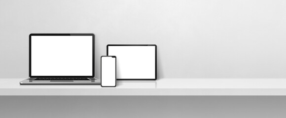 Laptop, mobile phone and digital tablet pc on white concrete wall shelf. Banner background