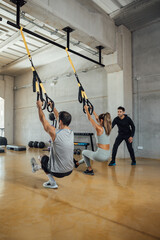 Fit man and woman train with suspension straps at gym with a personal trainer.