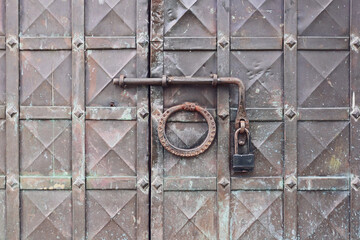 Antique wrought iron door knocker on an old metal door in Russian style.  The forged handle of the handmade hammer is made of iron close-up against the background of a metal door.       