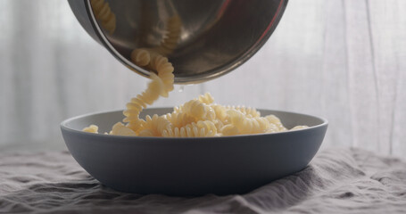 pour freshly cooked fusilli pasta in blue bowl