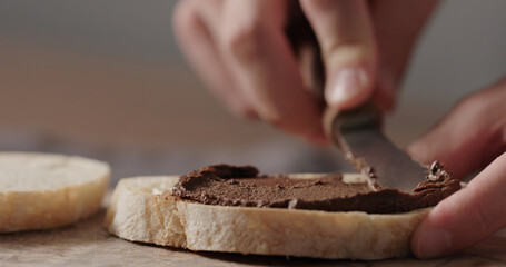 man spreading chocolate nut spread on ciabatta slice on olive board